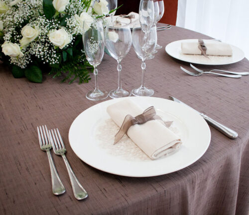 Un tavolo da ristorante è apparecchiato con tovaglia, stoviglie, bicchieri e un centro tavola floreale.