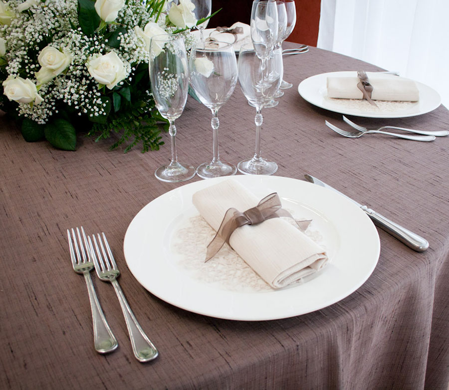 Un tavolo da ristorante è apparecchiato con tovaglia, stoviglie, bicchieri e un centro tavola floreale.