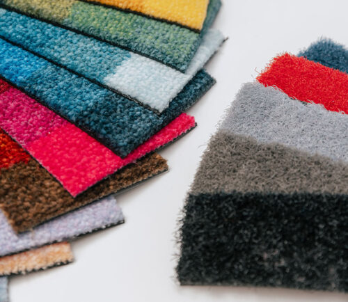 Diversi ritagli di materiale da tappeti di molti colori poggiano su un tavolo disposti a ventaglio.