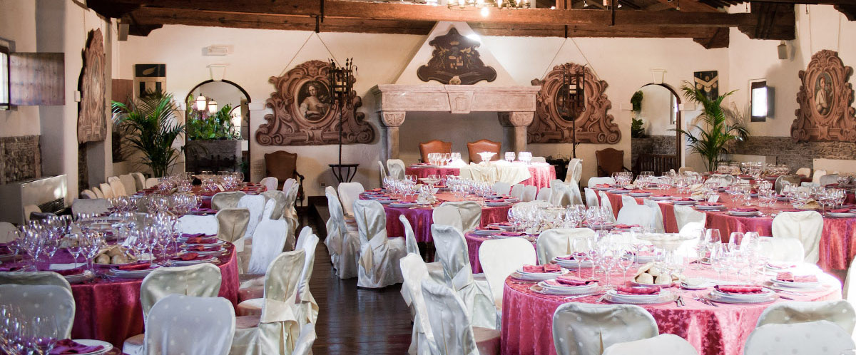 Sala di un locale allestita per un ricevimento, contenente svariati tavoli apparecchiati.