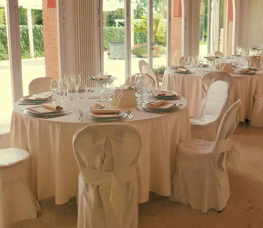 Vista di una sala in cui sono dei tavoli apparecchiati circondati da sedie rivestite di tessuto.