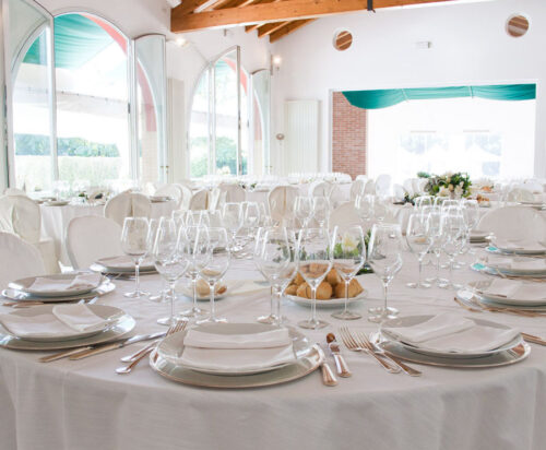 Primo piano di un tavolo apparecchiato con tovaglia, stoviglie, bicchieri e cibo.