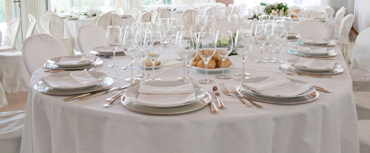 Primo piano di un tavolo apparecchiato con tovaglia, stoviglie, bicchieri e cibo.