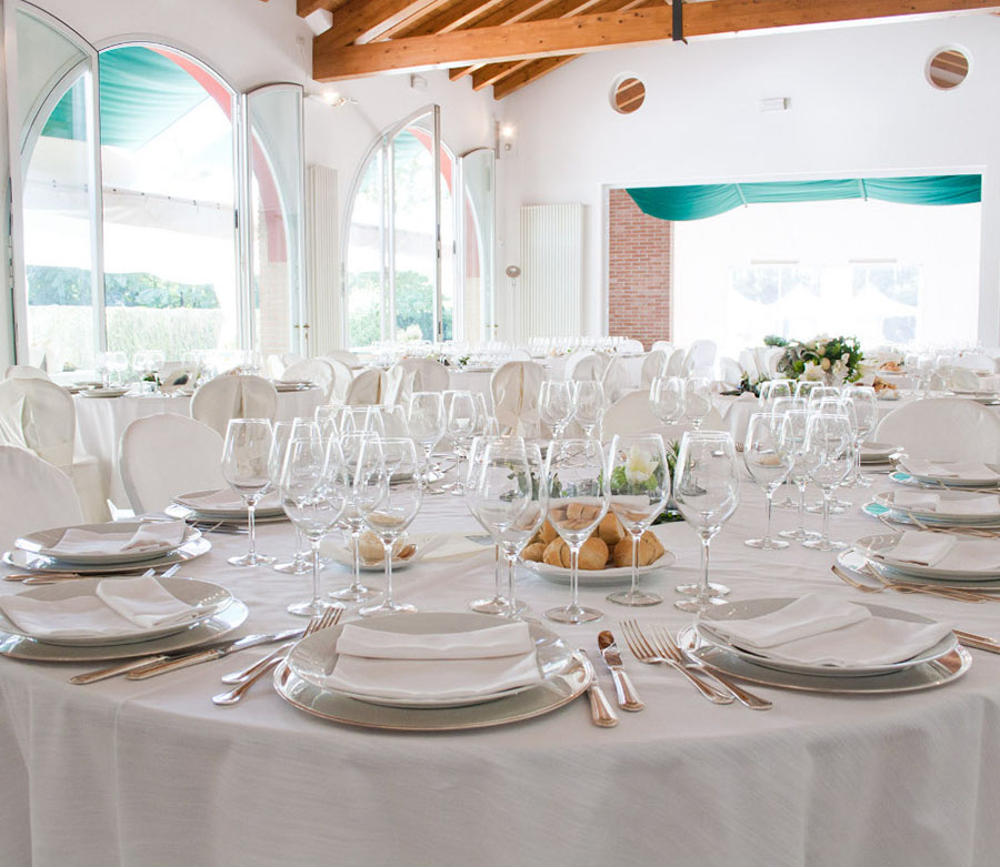 Primo piano di un tavolo apparecchiato con tovaglia, stoviglie, bicchieri e cibo.