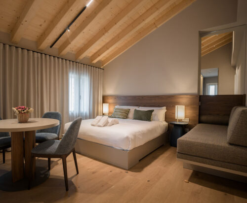 Camera d'hotel contenente un letto matrimoniale, tavolo con sedie e un divanetto angolare.