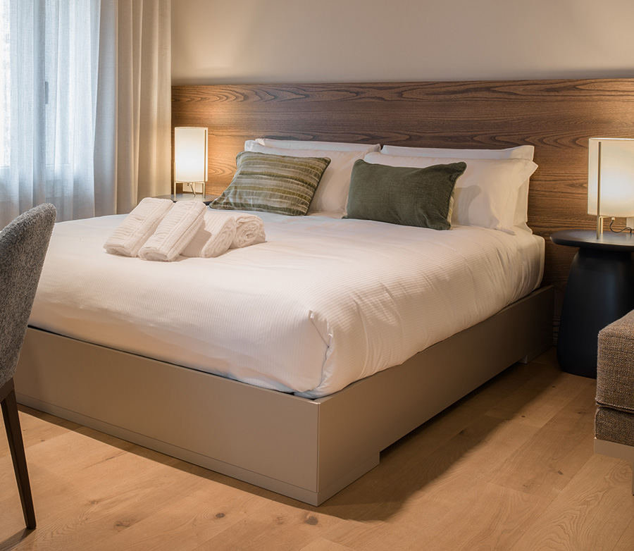 Dettaglio di una camera d'albergo con focus sul letto matrimoniale ai cui piedi poggiano degli asciugamani ripiegati.