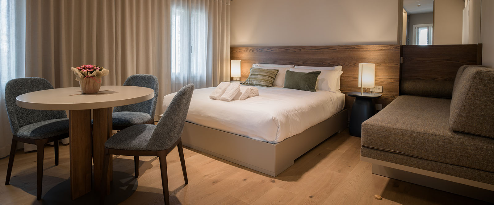 Camera d'hotel contenente un letto matrimoniale, tavolo con sedie e un divanetto angolare.