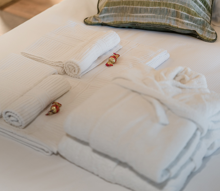 Dettaglio di un letto matrimoniale su cui poggiano degli asciugamani e degli accappatoi.