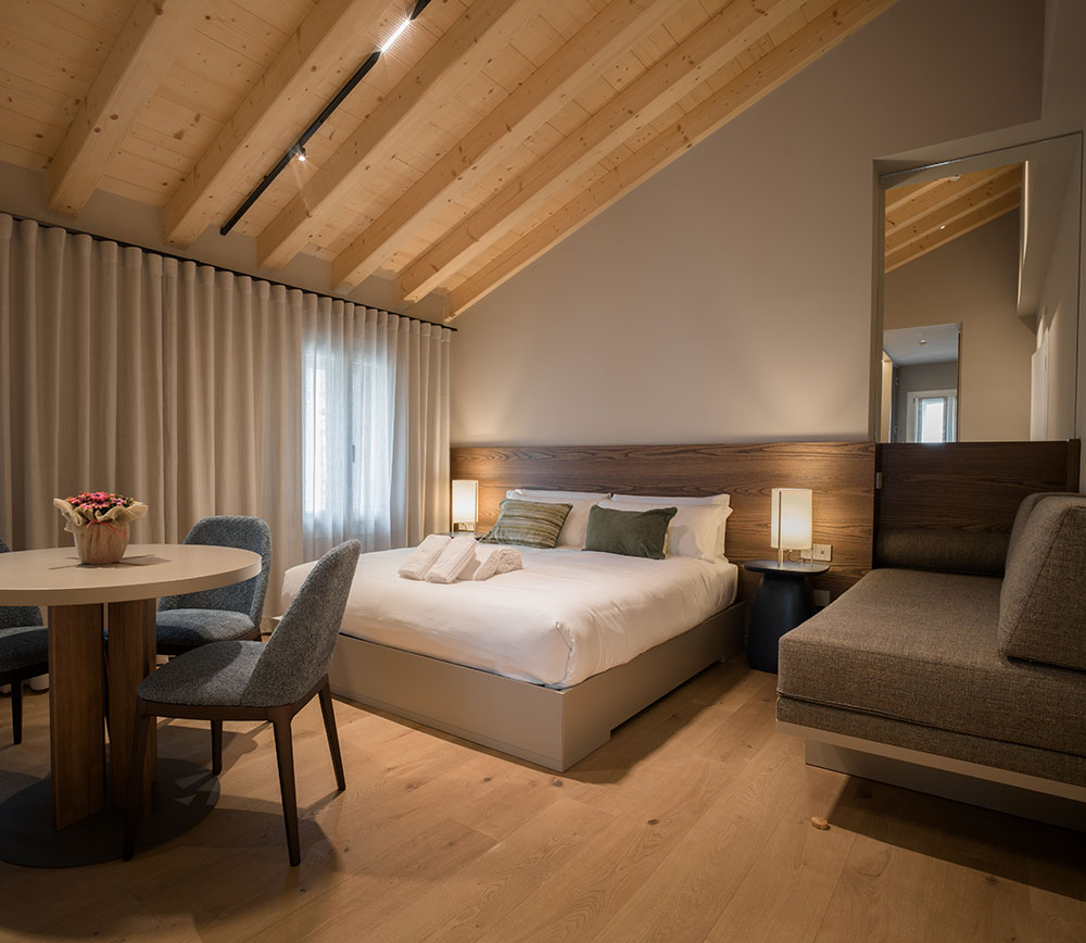 Camera d'hotel contenente un letto matrimoniale, tavolo con sedie e un divanetto angolare.