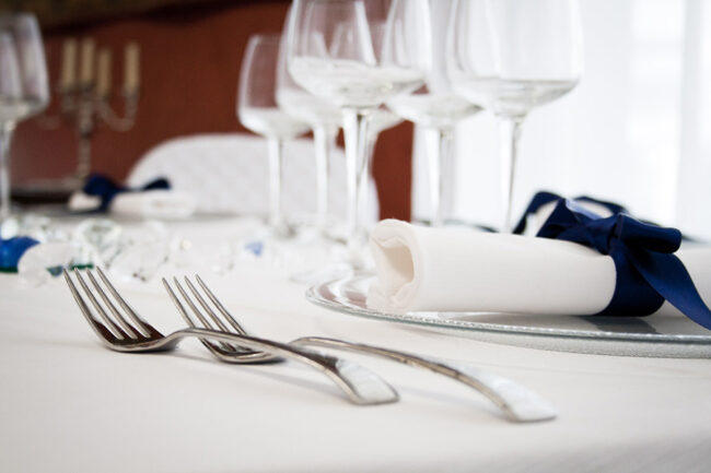 Dettaglio di una tavola apparecchiata con biancheria bianca.