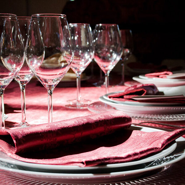 Dettaglio di una tavola apparecchiata con biancheria damascato rosso.
