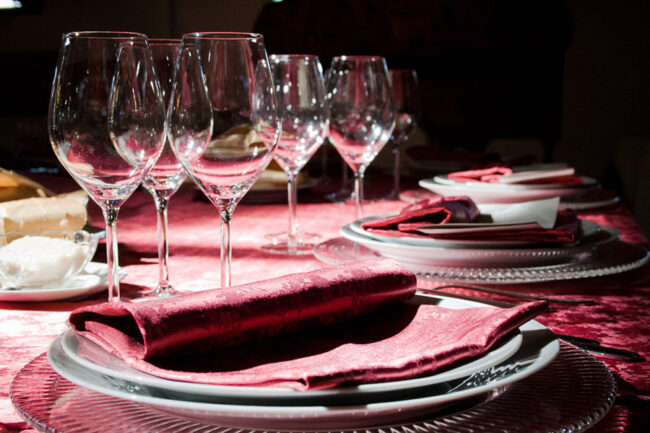 Dettaglio di una tavola apparecchiata con biancheria damascato rosso.