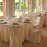 Dettaglio di una sala da pranzo con tavole apparecchiate con biancheria color avorio.