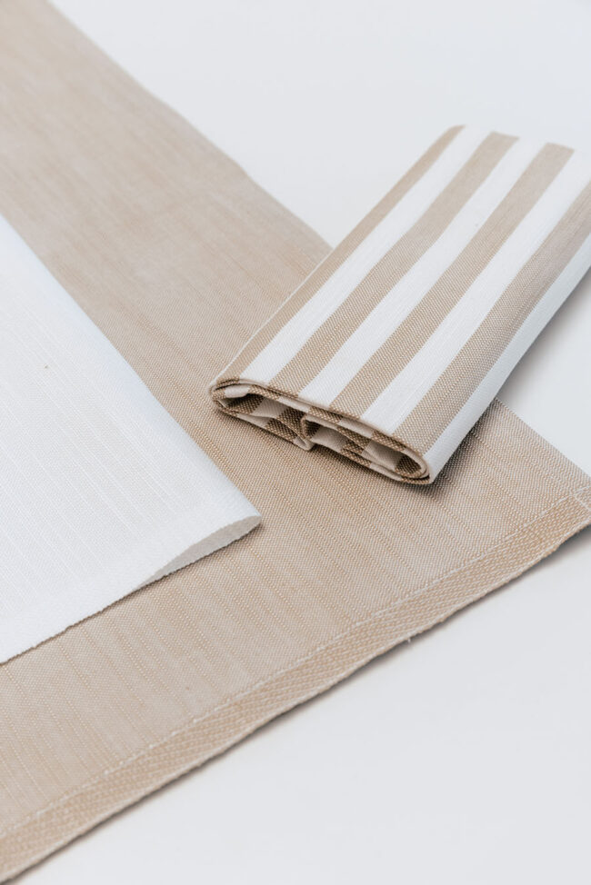 Dettaglio di un tovagliolo a righe marroni e beige posato su una tovaglia.