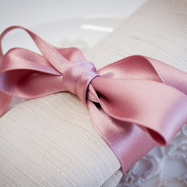 Dettaglio di un tovagliolo color avana legato da un nastro di raso rosa.