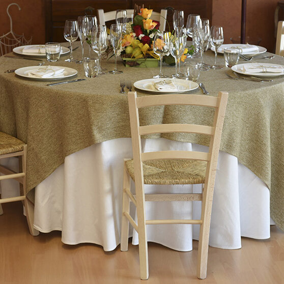 Vista frontale di una tavola apparecchiata con stoviglie, posate, bicchieri e una tovaglia color verde salvia.