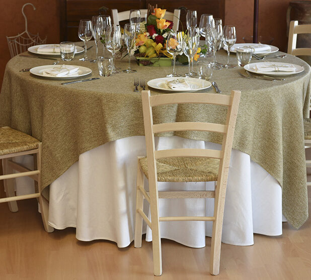 Vista frontale di una tavola apparecchiata con stoviglie, posate, bicchieri e una tovaglia color verde salvia.