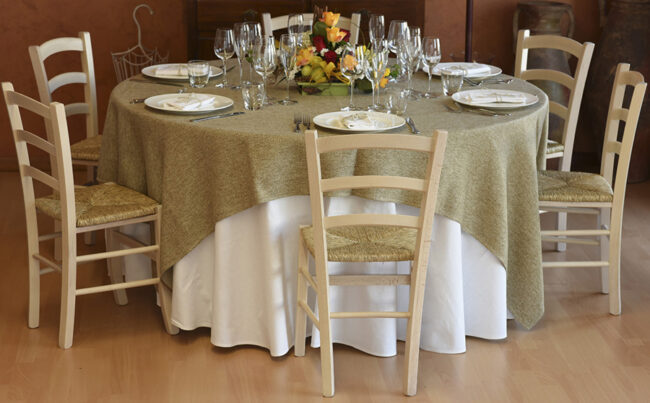 Vista frontale di una tavola apparecchiata con stoviglie, posate, bicchieri e una tovaglia color verde salvia.